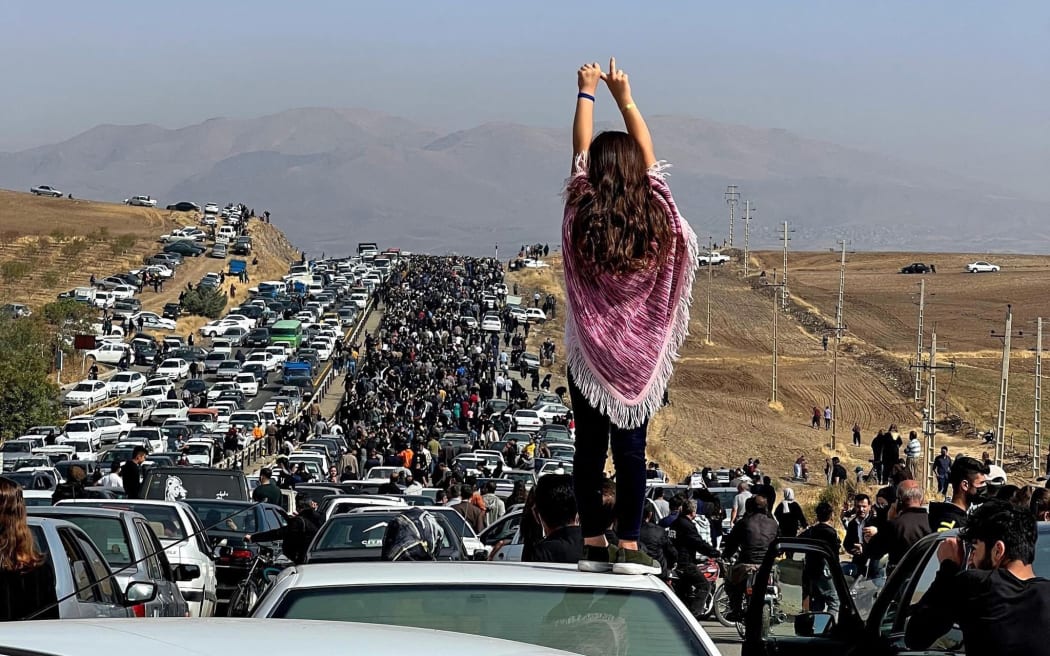 This UGC image posted on Twitter reportedly on October 26, 2022 shows an unveiled woman standing on top of a vehicle as thousands make their way towards Aichi cemetery in Saqez, Mahsa Amini's home town in the western Iranian province of Kurdistan, to mark 40 days since her death, defying heightened security measures as part of a bloody crackdown on women-led protests. - A wave of unrest has rocked Iran since 22-year-old Amini died on September 16 following her arrest by the morality police in Tehran for allegedly breaching the country's strict rules on hijab headscarves and modest clothing. (Photo by UGC / AFP) / === RESTRICTED TO EDITORIAL USE - MANDATORY CREDIT "AFP PHOTO / UGC IMAGE" - NO MARKETING NO ADVERTISING CAMPAIGNS - DISTRIBUTED AS A SERVICE TO CLIENTS FROM ALTERNATIVE SOURCES, AFP IS NOT RESPONSIBLE FOR ANY DIGITAL ALTERATIONS TO THE PICTURE'S EDITORIAL CONTENT, DATE AND...