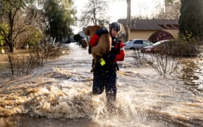 San Diego firefighter Brian Sanford rescues a dog from a flooded home in Merced, California, on January 10, 2023. - Relentless storms were ravaging California again Tuesday, the latest bout of extreme weather that has left 14 people dead. Fierce storms caused flash flooding, closed key highways, toppled trees and swept away drivers and passengers -- reportedly including a five-year-old-boy who remains missing in central California. (Photo by JOSH EDELSON / AFP)