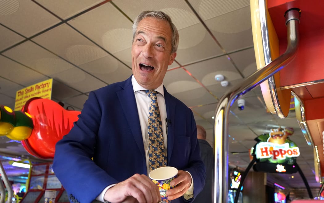 Britain's Nigel Farage, Reform UK party leader plays on a game in an amusement arcade holds out some coins whilst spending time with supporters in Clacton-On-Sea, Essex, England Friday, 21 June, 2024.