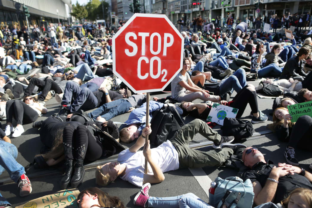 20 September 2019, North Rhine-Westphalia, Duesseldorf: Participants in a demonstration lie at a crossroads. A demonstrator holds up his poster "Stop CO2".