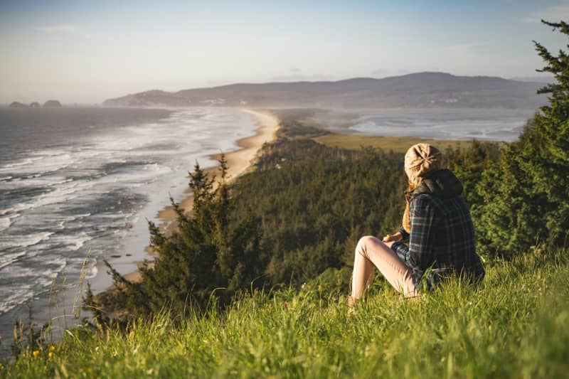 Person sitting on a grassy hill overlooking a coastline.