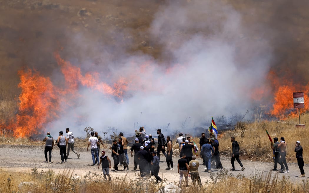 Members of Syria's Druze community walk through tear gas fumes released by Israeli forces to disperse them, as they gather along the dividing line to attempt to cross the barbed-wire fence with the Israeli-annexed Golan Heights near Majdal Shams on July 16, 2025. Israeli troops on July 16 sought to control crowds and prevent Druze from crossing the border with Syria, after deadly violence in the country's south that prompted Damascus to send in government forces. (Photo by Jalaa MAREY / AFP)