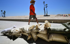 A man walks past sand bags placed to protect beach front homes in Seal Beach, California on August 18, 2023, as they prepare for hurricane Hilary. Hilary strengthened into a Category 4 hurricane on August 18, 2023 and was expected to further intensify before approaching Mexico's Baja California peninsula over the weekend, the US National Hurricane Center (NHC) said. In the US, parts of southern California and southern Nevada could see heavy rain through early next week, the NHC said. (Photo by Frederic J. BROWN / AFP)