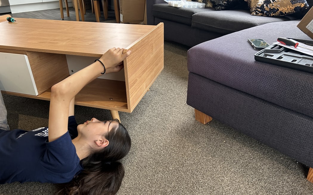 Picture of a young woman lying on the ground and fixing a furniture piece.