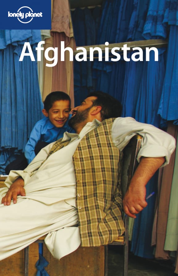 A retro magazine cover. A man in a plaid vest sits on a chair, laughing with a small boy behind him. In the background are racks full of blue dresses. The cover reads "AFGHANISTAN", and there is a "LONELY PLANET" logo in the upper left corner.