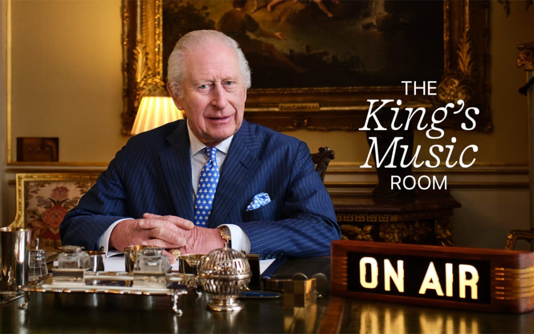 King Charles sits in his office in Buckingham Palace, an 'ON AIR' sign to his right and a graphic reading 'The King's Music Room' next to him.