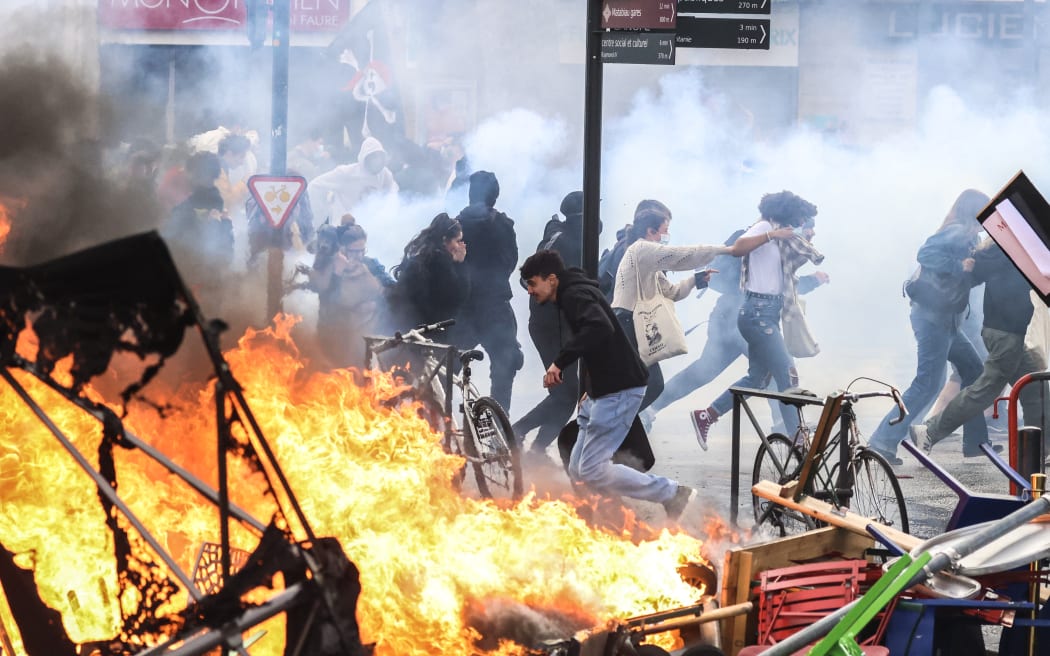 Protesters run in tear gas smoke next to   a street fire on the sidelines of a demonstration as part of a national day of strikes and protests, a week after the French government pushed a pensions reform through parliament without a vote, using the article 49.3 of the constitution, in Toulouse, southern France, on March 23, 2023. - French unions on March 23 staged a new day of disruption against the president's pension reform after he defiantly vowed to implement the change, which includes raising the age of retirement from 62 to 64, saying he was prepared to accept unpopularity in the face of sometimes violent protests. (Photo by Charly TRIBALLEAU / AFP)