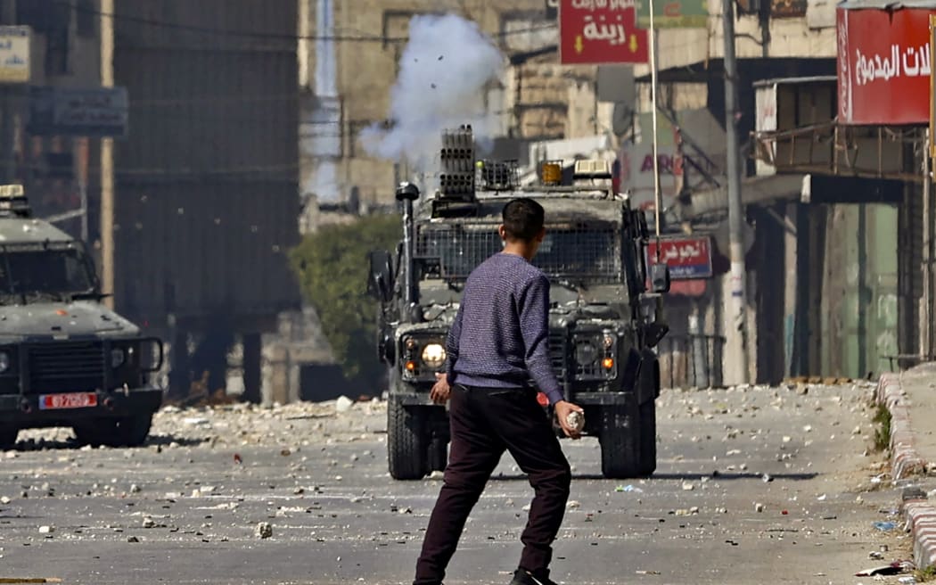 A Palestinian youth holds a rock as he faces an Israeli military vehicle, during a raid on the occupied-West Bank city of Nablus, on 22 February 2023.