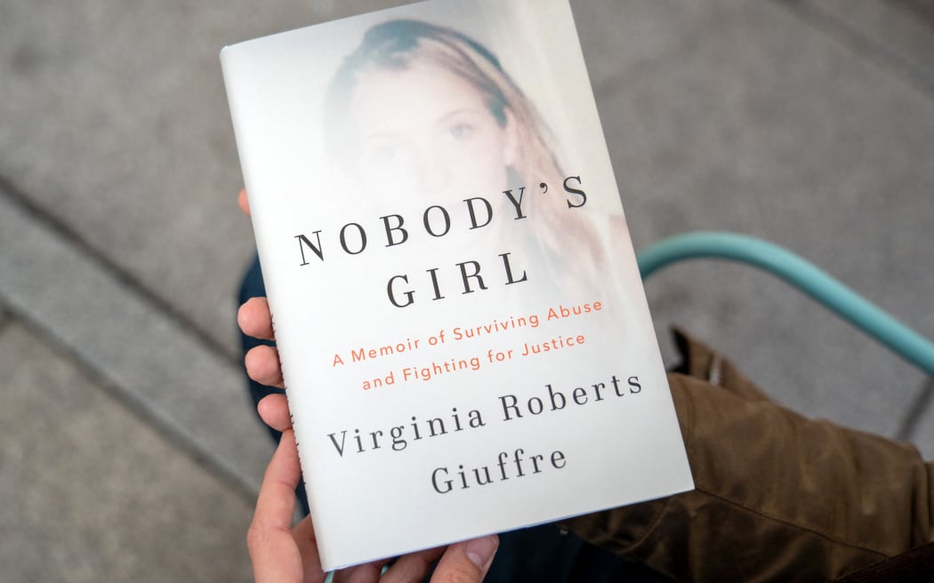 A person poses for a photo with a copy of the book "Nobody's Girl - A Memoir of Surviving Abuse and Fighting for Justice" by Virginia Roberts Giuffre, in central London on October 21, 2025, on the day of its release in the UK. A memoir by one of Jeffrey Epstein's main accusers whose claims led to the downfall of Britain's Prince Andrew was released Tuesday, promising to keep Epstein's ties to President Donald Trump in the spotlight. (Photo by Niklas HALLE'N / AFP)