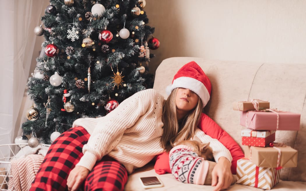 Woman falling asleep and tired of gift wrapping with puppy dog on a couch in the living room with Christmas tree at home