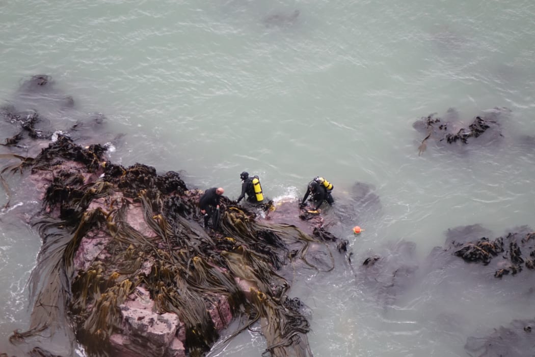 Police divers can be seen on the rocks near the site of the underwater wreck.