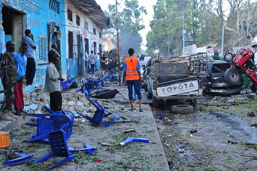 People stand among damages at the scene of a blast after two car bombs exploded in Mogadishu on October 28, 2017.