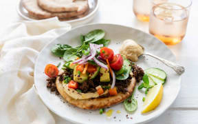 Spiced lamb mince with hummus and flatbreads on a round white plate garnished with herbs and a lemon wedge.