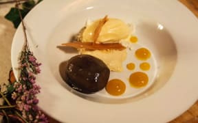 A white plate, featuring finely presented honey products. Two scoops of icecream, with blobs of honey, and shards of honeycomb.