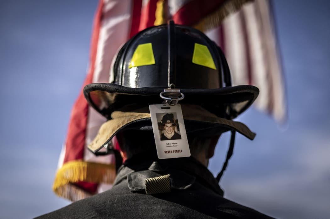 A firefighter wearing the photo badge of a victim on his helmet, pauses for a moment of silence on September 11, 2021 in  Morrison, outside Denver, Colorado.