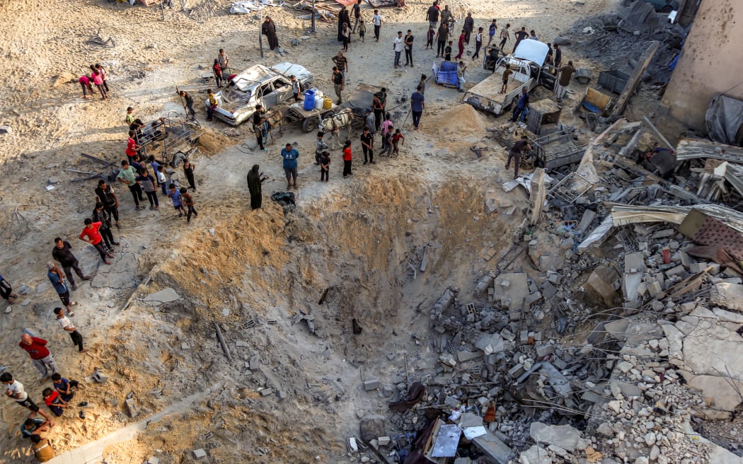 People gather around an impact crater by a destroyed building in the aftermath of overnight Israeli bombardment in the Japanese neighbourhood in the northwest of Khan Yunis in the southern Gaza Strip on July 28, 2025. (Photo by AFP)
