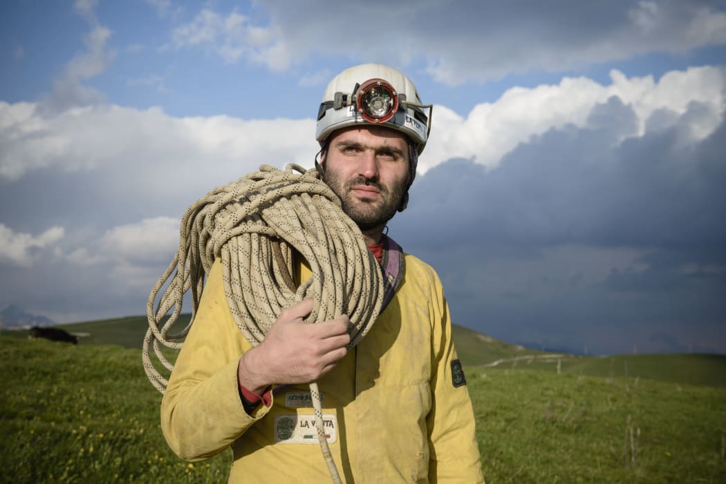 Cave explorer Francisco Sauro wearing a safety helmet with a headlamp. He is carrying a length of rope and is dressed in overalls