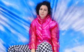 Young woman with dark curly hair wearing a bright pink jacket and black and white chequered pants