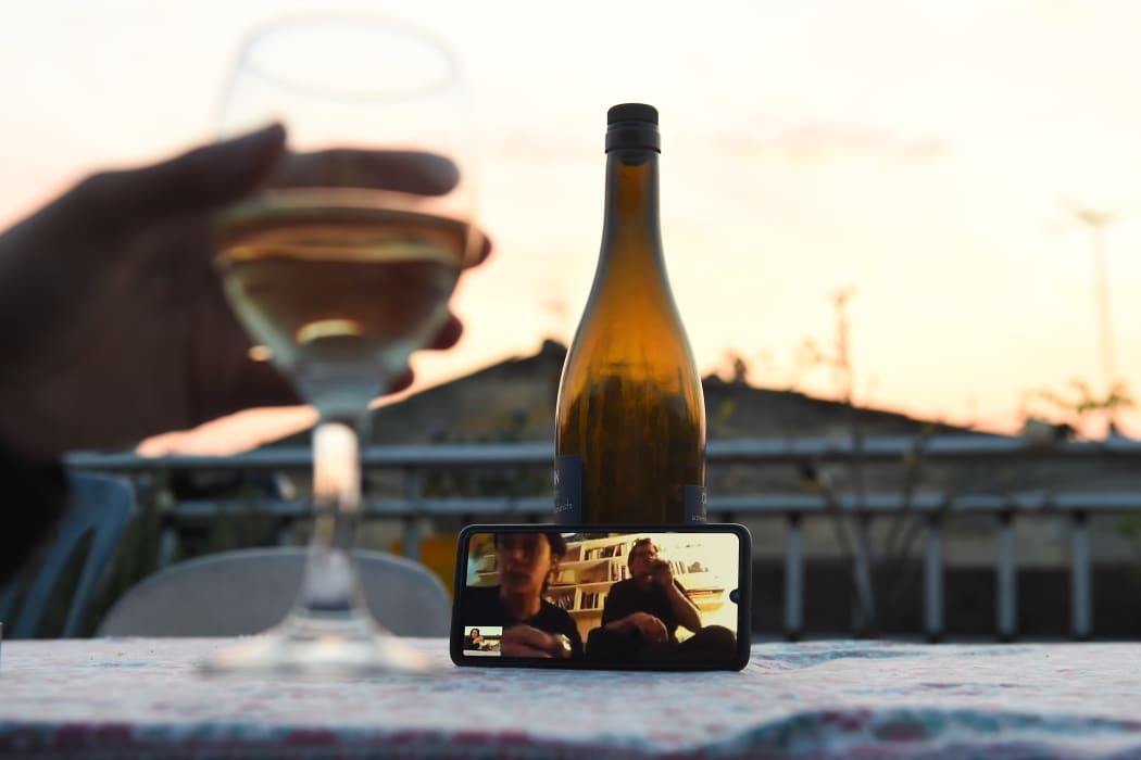 A woman drinks a glass of wine as she speaks and shares a drink with friends via a video call.