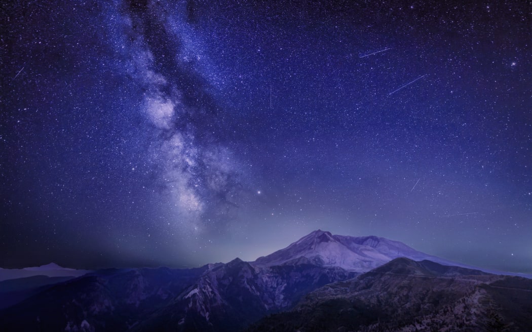 The Delta Aquariids meteor shower and Milky Way over Mount St. Helens, at Windy Ridge in Washington State with Mt. Hood, Oregon visible in the lower left corner.  Portland, Oregon is fifty miles to the south as you can tell by the ambient light behind Mount St. Helens.
