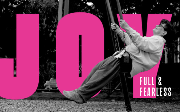 A black-and-white image of a smiling Joy Cowley sitting on a swing. Large text in the background of the image reads: "Joy Full & Fearless."