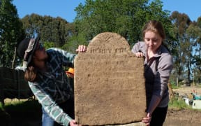 The headstone for Henry Pim held up by archaeology students Teina Tutaki and Alana Kelly