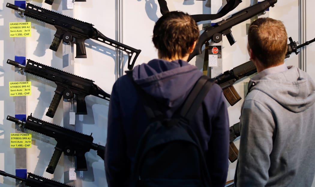 (FILES) In this file photo taken on March 29, 2019, visitors look at semi-automatic shotguns displayed on a wall during the 45th edition of the Arms Trade Fair, in Lucerne.