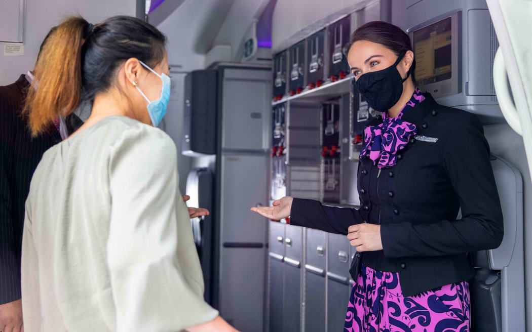 A flight attendant welcomes passengers onto an Air New Zealand flight.