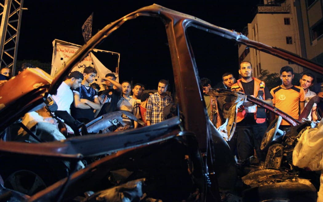 People gather around the wreckage of a car after it was hit by an Israeli strike in Gaza city.