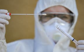 A medical assistant in protective equipment holds a test for the coronavirus Sars-Cov-2 in her hands.