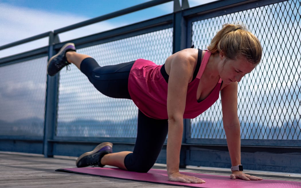 A woman exercising outdoors on a yoga mat.