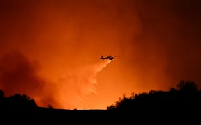 A helicopter drops water on smoke and flames from the Palisades Fire burning behind Mulholland drive towards the Encino neighborhood in Los Angeles, California, January 10, 2025. Massive wildfires that engulfed whole neighborhoods and displaced thousands in Los Angeles have killed at least 10 people, authorities said, as California's National Guard soldiers readied to hit the streets to help quell disorder.
News of the growing toll, announced late Thursday January 9 by the Los Angeles County Medical Examiner, came as swaths of the United States' second-largest city lay in ruins. (Photo by Patrick T. Fallon / AFP)