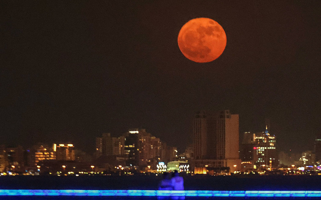 People watch as the "buck moon" rises over the skyline of Kuwait City on July 3, 2023. (Photo by YASSER AL-ZAYYAT / AFP)