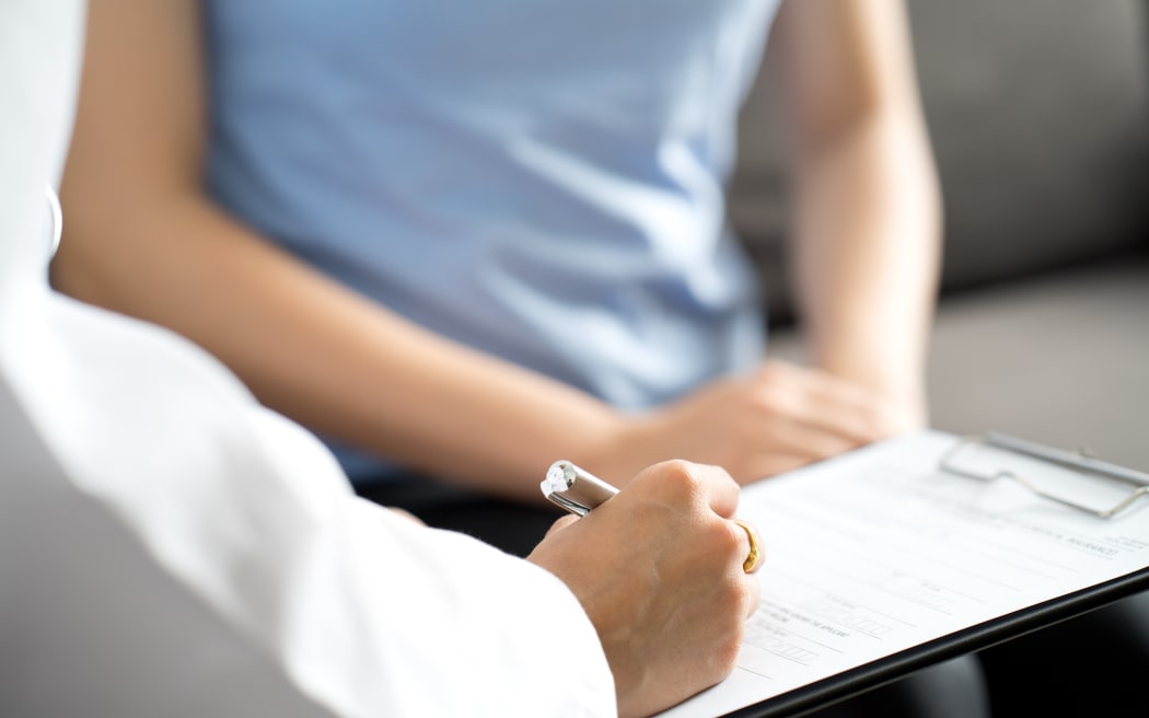 A medical professional takes notes while talking to a female patient.