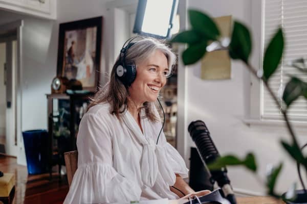 Petra sits at a desk with headphones on, speaking into a microphone and smiling.