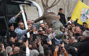 A man jumps to greet a former Palestinian prisoner released by Israel as he and others disembark a Red Cross bus after arriving in Ramallah, in the occupied West Bank on February 1, 2025. The inmates departed from the Israeli prison in the occupied West Bank after three Israeli hostages were handed over by Hamas in Gaza in a fourth such exchange agreed under the ceasefire deal. (Photo by Ahmad GHARABLI / AFP)