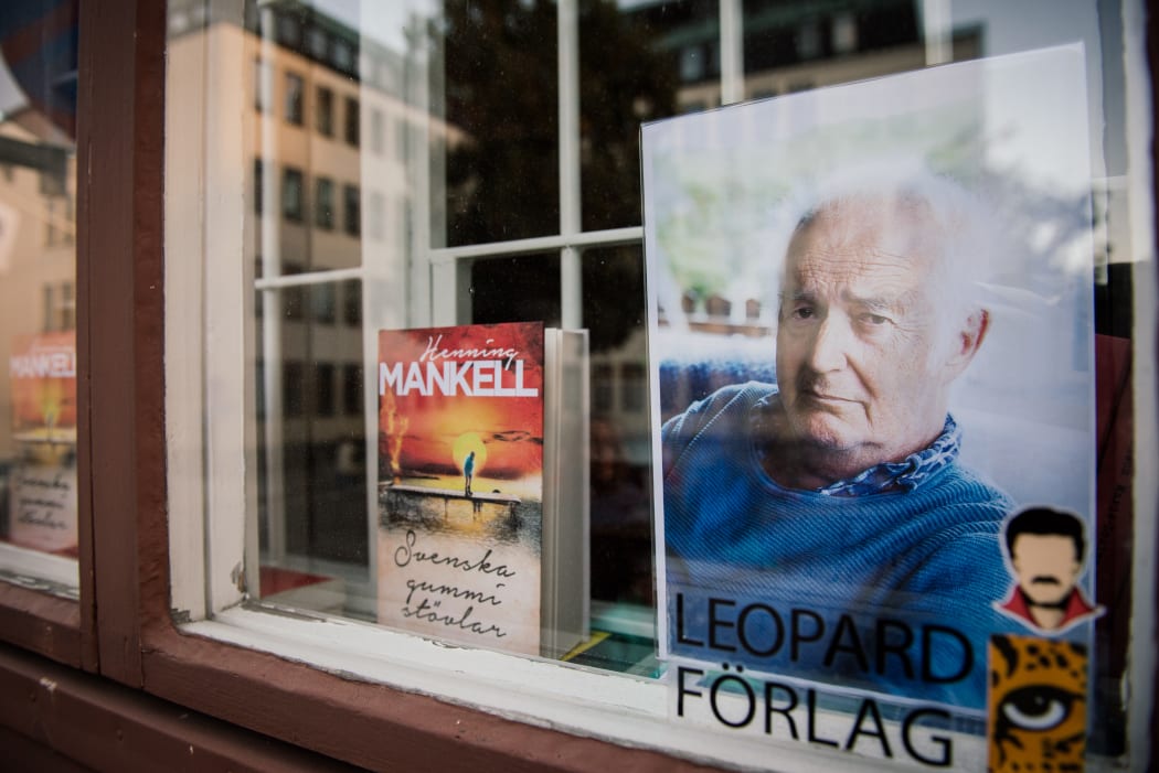 A picture of Swedish crime writer Henning Mankell and copies of some of his books are displayed inside a window of a Swedish publishing company.