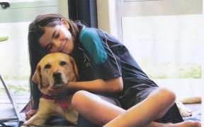 Greta lies on a blanket in a library. A young girl cuddles Greta, smiling.