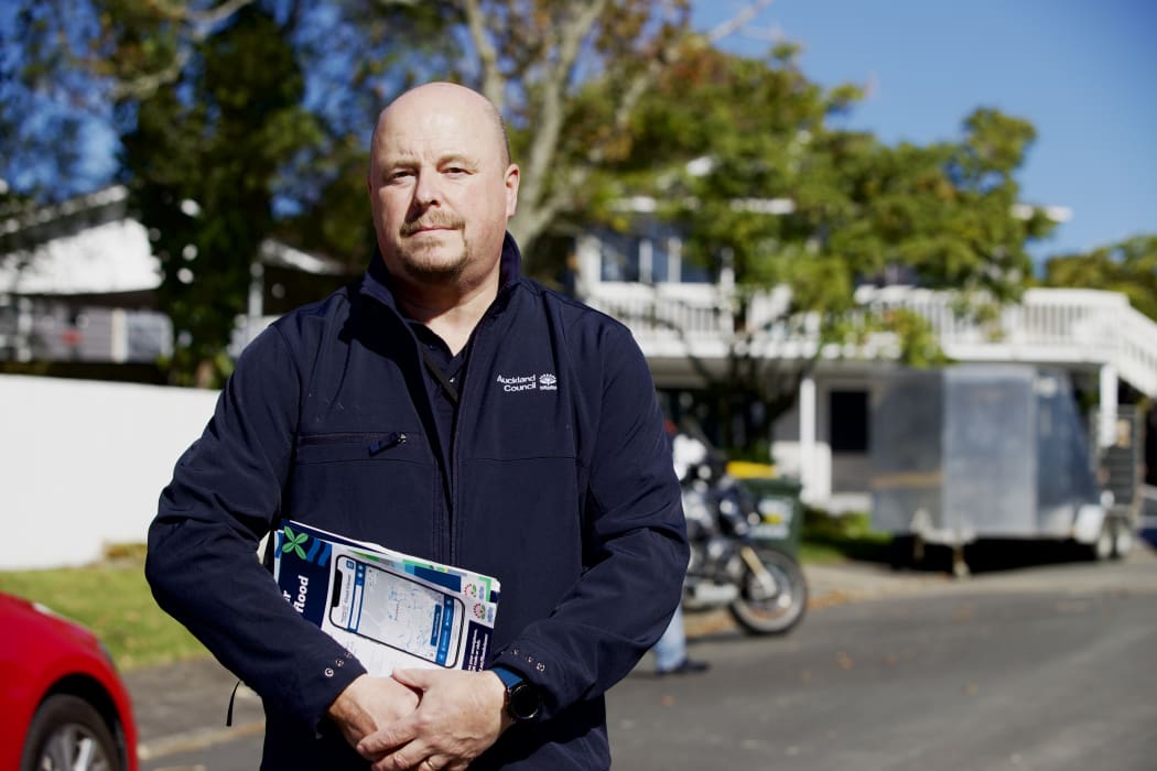 Compliance Manager Adrian Wilson stands in the middle of a street holding documents.