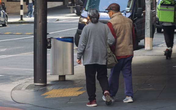 An elderly Chinese couple crossing the road on Queen Street in Auckland City.