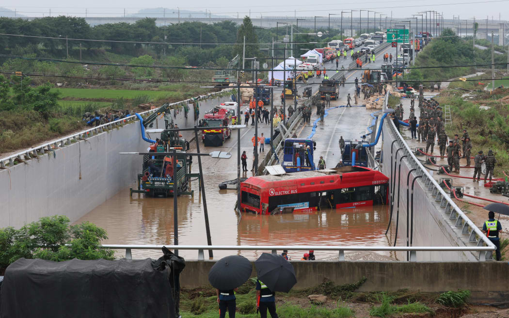 South Korean rescue workers search for missing persons near a bus along a deluged road leading to an underground tunnel where some 15 cars were trapped in flood waters after heavy rains in Cheongju.