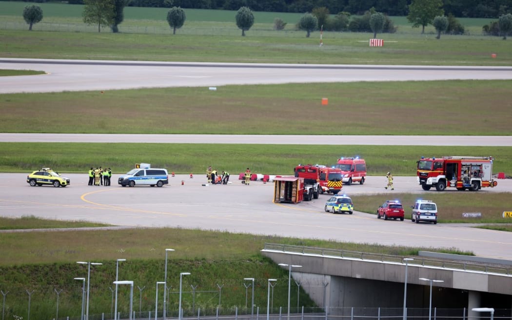 18 May 2024, Bavaria, Munich: Police and firefighters stand on a runway access road at Franz-Josef-Strauß Airport around climate activists who have stuck themselves there.  Climate protection activists paralyzed Munich Airport early Saturday morning. The activists had reached the inner area of the airport grounds. According to their own statements, members of the so-called Last Generation had planned to enter the airport grounds in order to block at least one of the two runways. Photo: Karl-Josef Hildenbrand/dpa (Photo by KARL-JOSEF HILDENBRAND / DPA / dpa Picture-Alliance via AFP)