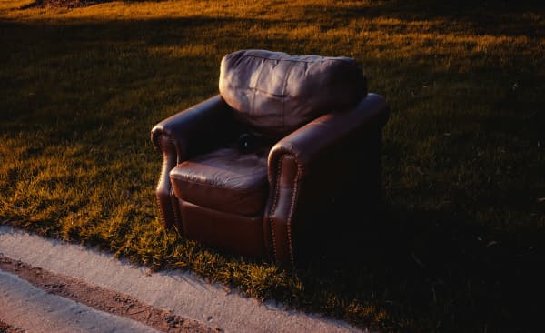 A leather couch chair thrown out on the side of the road.