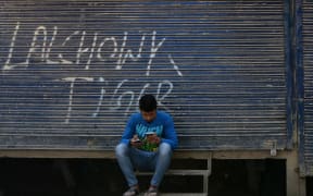A Kashmiri man looks at his mobile phones in front of shuttered shops in Srinagar.