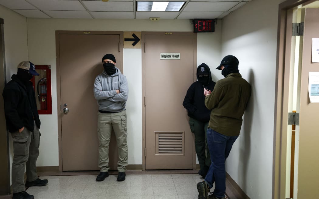 Masked federal agents stand in a hallway at the New York Federal Plaza Immigration Court inside the Jacob K. Javitz Federal Building in New York on December 22, 2025. US President Donald Trump has made deporting undocumented immigrants a key priority for his second term, after successfully campaigning against an alleged "invasion" by criminals. (Photo by CHARLY TRIBALLEAU / AFP)