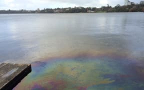 Rainbow coloured diesel stains the lake in the foreground while houses can be seen in the background