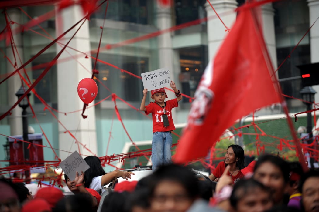 A young boy holds a sign reading 'Damn decree' in reference to the state of emergency in Thailand.