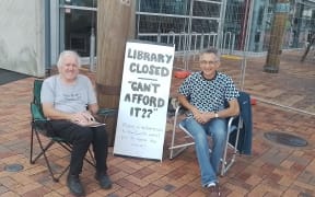 Whangārei’s Brian Cox (left) and Greg Waite protesting outside the library's shut front doors on the first day of its Sunday closures, the scaffolding behind them for maintenance of the building's skylight