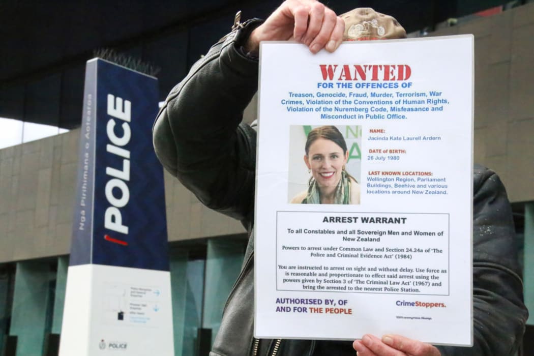 An anti-mandate protester outside Christchurch central police station holds up a fake arrest warrant for Prime Minister Jacinda Ardern.