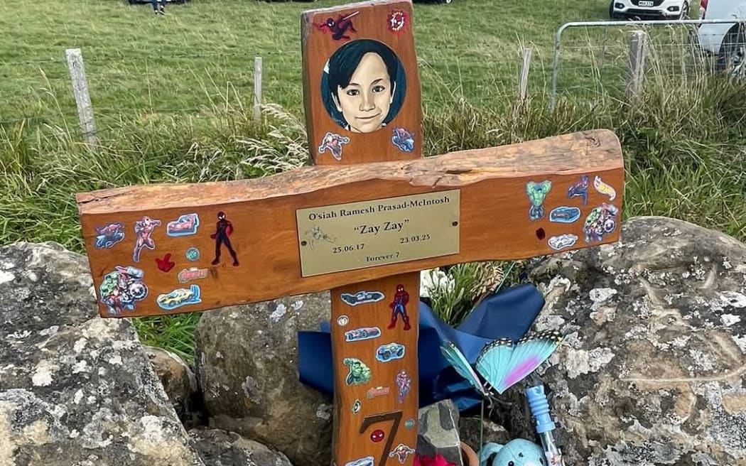 A memorial cross for O'siah Prasad covered in stickers, toys and flowers.